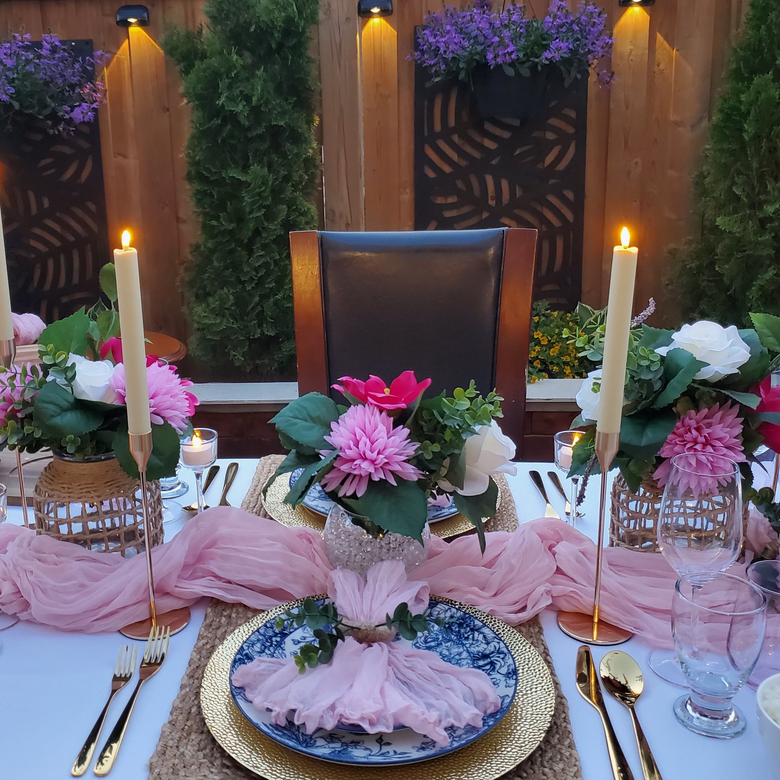 Elegant outdoor dinner table setting with pink tablecloth, candles, and floral arrangements.