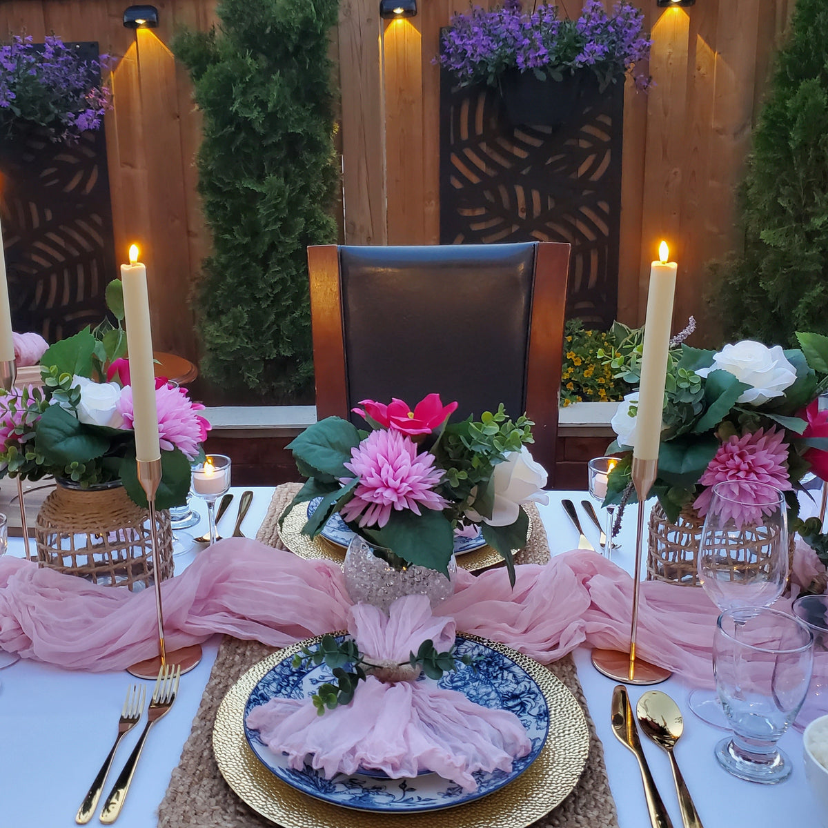 Elegant outdoor dinner table setting with pink tablecloth, candles, and floral arrangements.