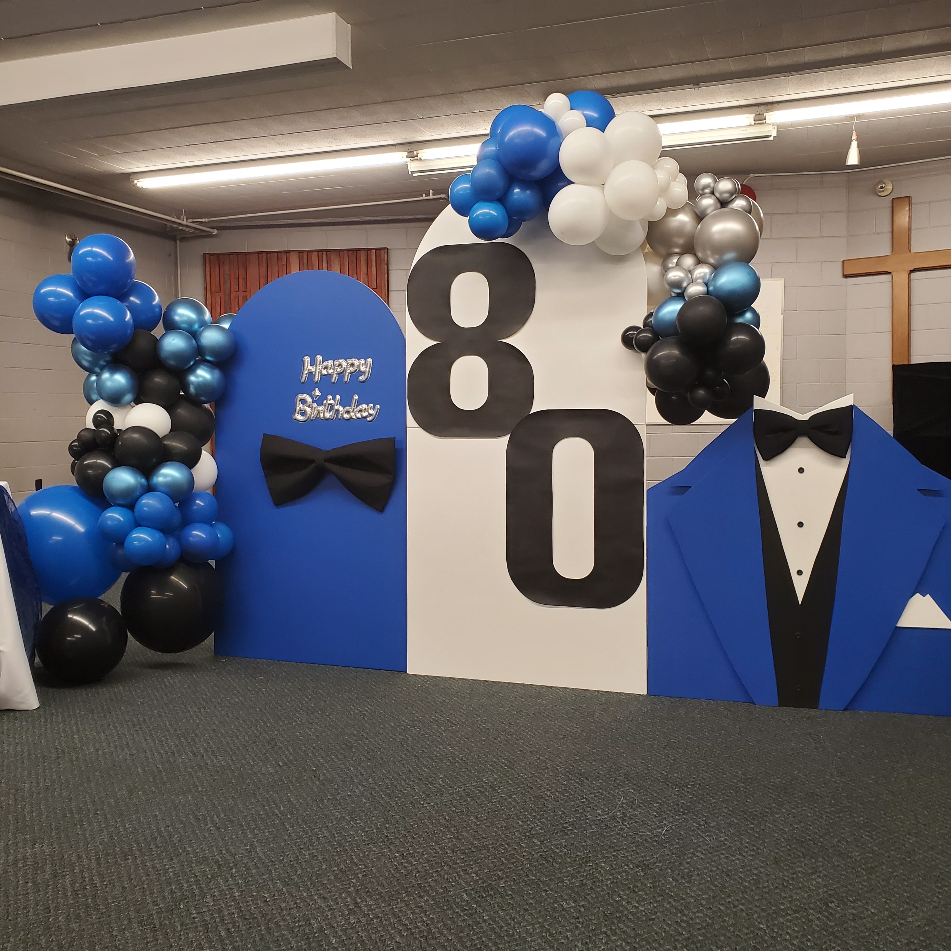Decorative setup for a 80th birthday party with balloons, a blue suit, and 'Happy Birthday' text.