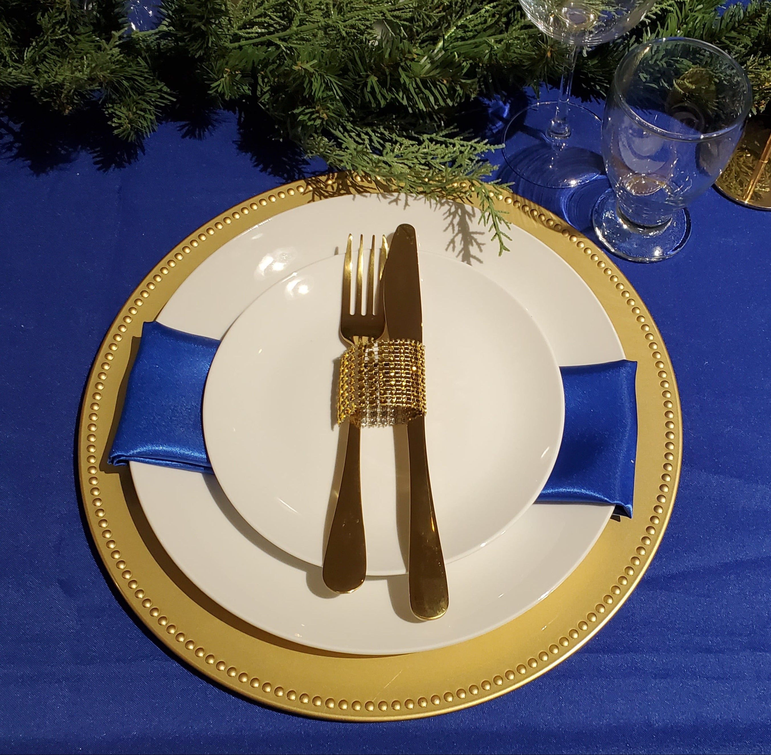 Elegant table setting with gold cutlery, white plates, and blue napkins on a blue tablecloth.